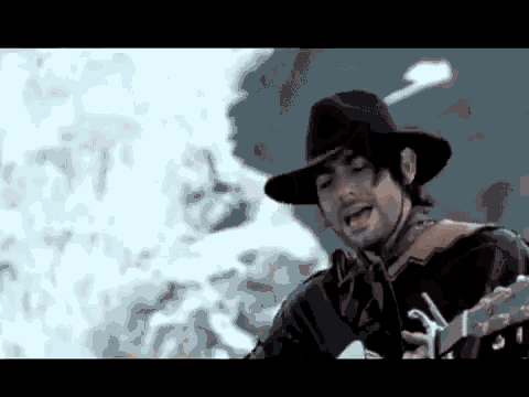 a man in a cowboy hat is holding a guitar in front of a fire .