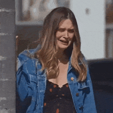 the woman is wearing a denim jacket and a black dress and is crying .
