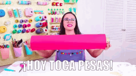 a woman is holding a pink roll of paper and the words hoy toca pesas are above her