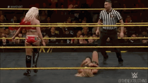 a woman is laying on the ground in a wrestling ring while a referee stands behind her