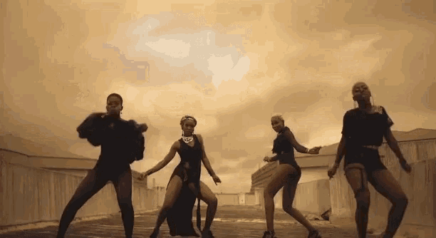a group of women are dancing on a street with a cloudy sky behind them