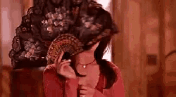 a woman in a red dress is holding a fan in front of her face .