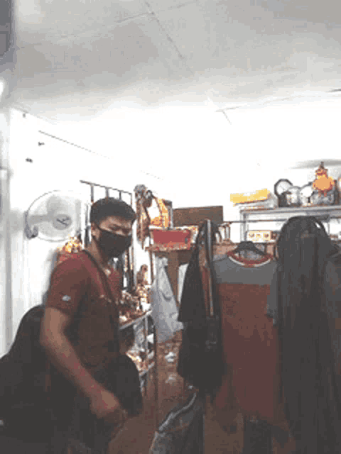 a man wearing a mask is standing in a room with clothes hanging