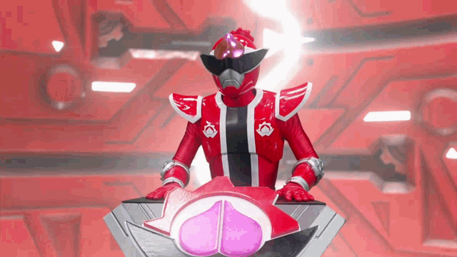 a red superhero is standing on a podium with a pink heart in front of him
