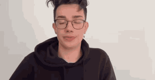 a young man wearing glasses and a black hoodie with his eyes closed .