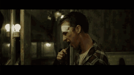 a man with a bandage on his forehead looks at his reflection in the mirror