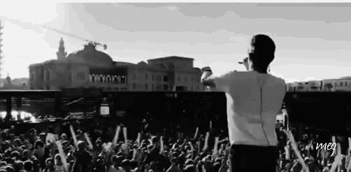 a black and white photo of a man standing in front of a crowd with the word meg on the bottom right