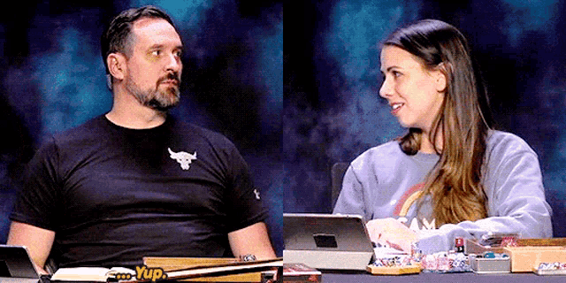 a man and a woman are sitting at a table and the man is wearing a black shirt with a bull on the front
