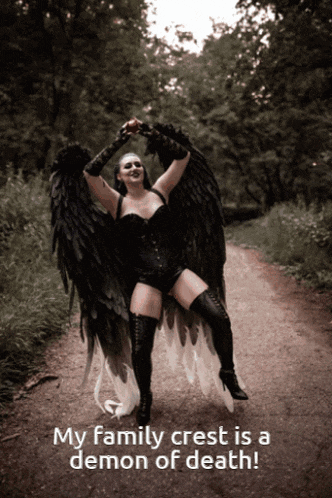 a woman in a black angel costume stands on a dirt road