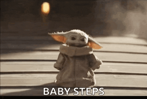 a baby yoda doll is standing on a wooden floor and says `` baby steps '' .