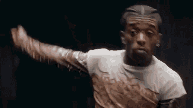 a man in a white t-shirt is dancing in a dark room with his arm outstretched .