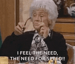 an elderly woman is sitting at a table holding glasses and saying `` i feel the need , the need for speed !! ''
