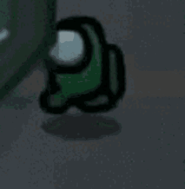 a green among us character is standing on a concrete floor .