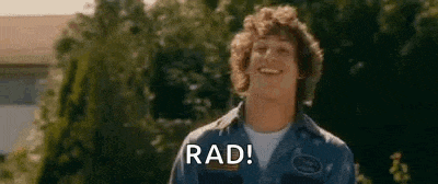 a young man is smiling and saying `` rad '' while standing in front of trees .