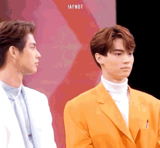 two men are standing next to each other and one is wearing an orange suit .