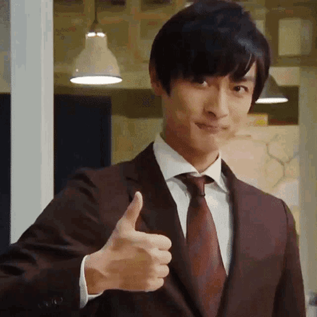 a man in a suit and tie is giving a thumbs up sign .
