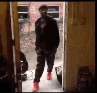 a man in a black jacket and red shoes stands in a doorway