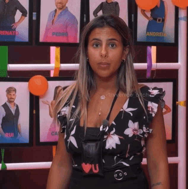 a woman in a floral top is standing in front of a wall with pictures of people including renato and andreia