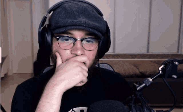 a man wearing headphones and a hat has his hand on his mouth