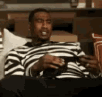 a man in a black and white striped shirt is sitting on a couch holding a cup of coffee .