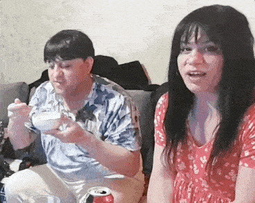 a man and a woman are sitting on a couch eating food and drinking soda