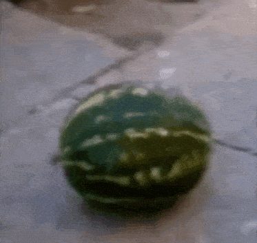 a watermelon is sitting on a concrete surface in a blurry photo