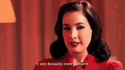 a woman in a red dress is standing in front of a lamp and saying `` i see beauty everywhere '' .