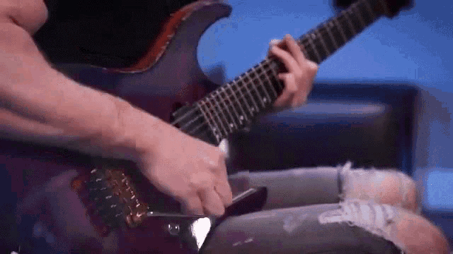 a man is playing an electric guitar while sitting on a couch