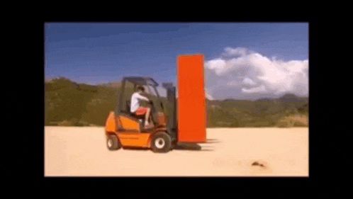 a man is driving a forklift carrying a large orange box .