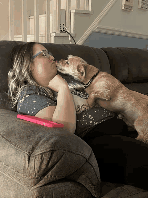 a woman laying on a couch with a dog licking her cheek