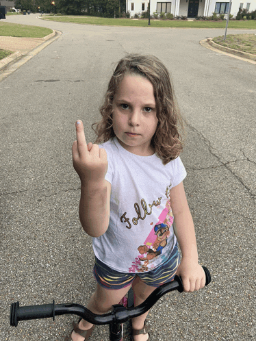 a little girl wearing a shirt that says " follow " is giving the middle finger