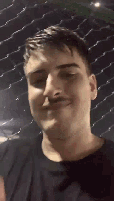 a man with a mustache is smiling in front of a fence