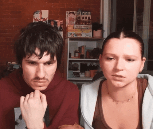 a man and a woman sitting in front of a shelf with a board game called ticket to ride