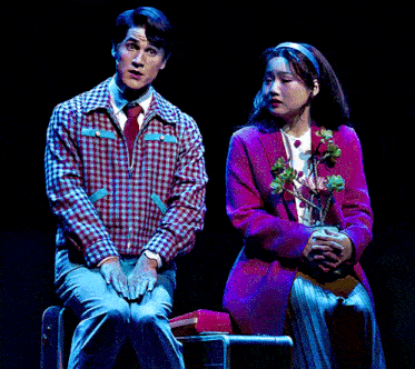 a man in a plaid jacket sits next to a woman in a pink coat