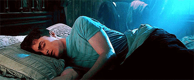 a man in a blue shirt is sleeping on a bed in a dark room
