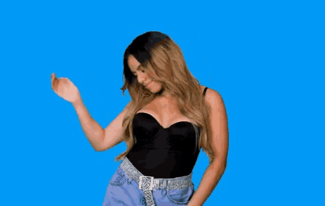 a woman in a black top is standing in front of a blue background and touching her hair .