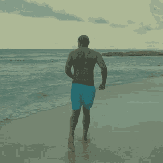 a man walking on a beach with a tattoo on his back that says jesus