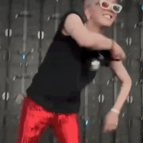 a man wearing a black tank top and red pants is dancing in front of a wall .