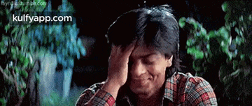 a man in a plaid shirt is holding his head with his hand .