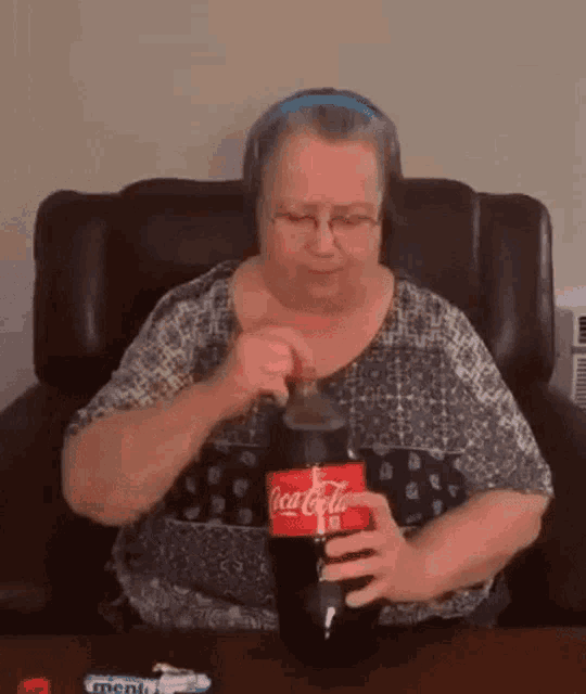 an older woman is sitting in a chair holding a bottle of coca cola .