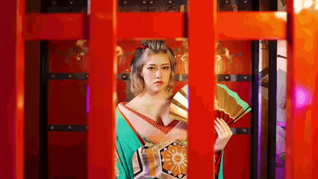 a woman in a kimono is holding a fan behind a fence