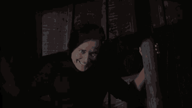 a man in a suit is standing in a dark room holding onto a wooden wall .