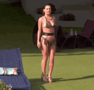 a woman in a bikini is standing on a lawn in front of a swimming pool .