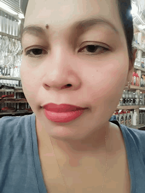 a woman wearing a blue shirt and red lipstick stands in front of a shelf of bottles
