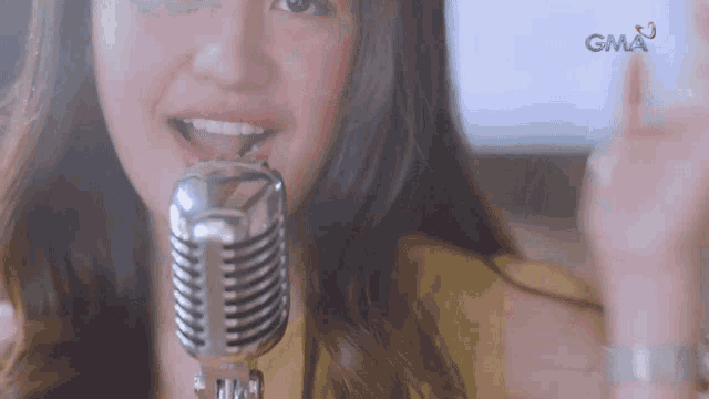 a close up of a woman singing into a microphone with gma in the background