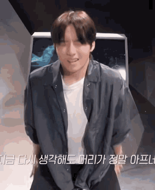 a man in a white shirt and a black jacket stands in front of a screen that says ' korean ' on it