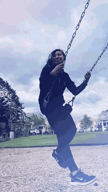 a woman wearing nike shoes is swinging on a swing
