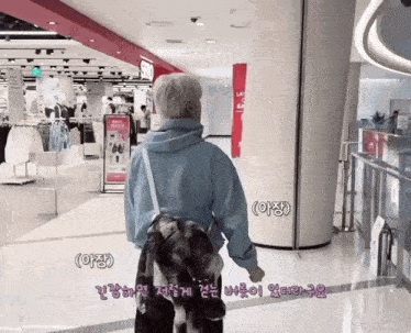 a man in a blue hoodie is walking down a hallway in a shopping mall .