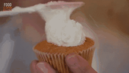 a close up of a person holding a cupcake with frosting and the words food tube on the bottom