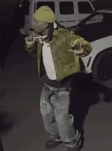 a man in a yellow jacket and hat is smoking a cigarette in front of a white car .